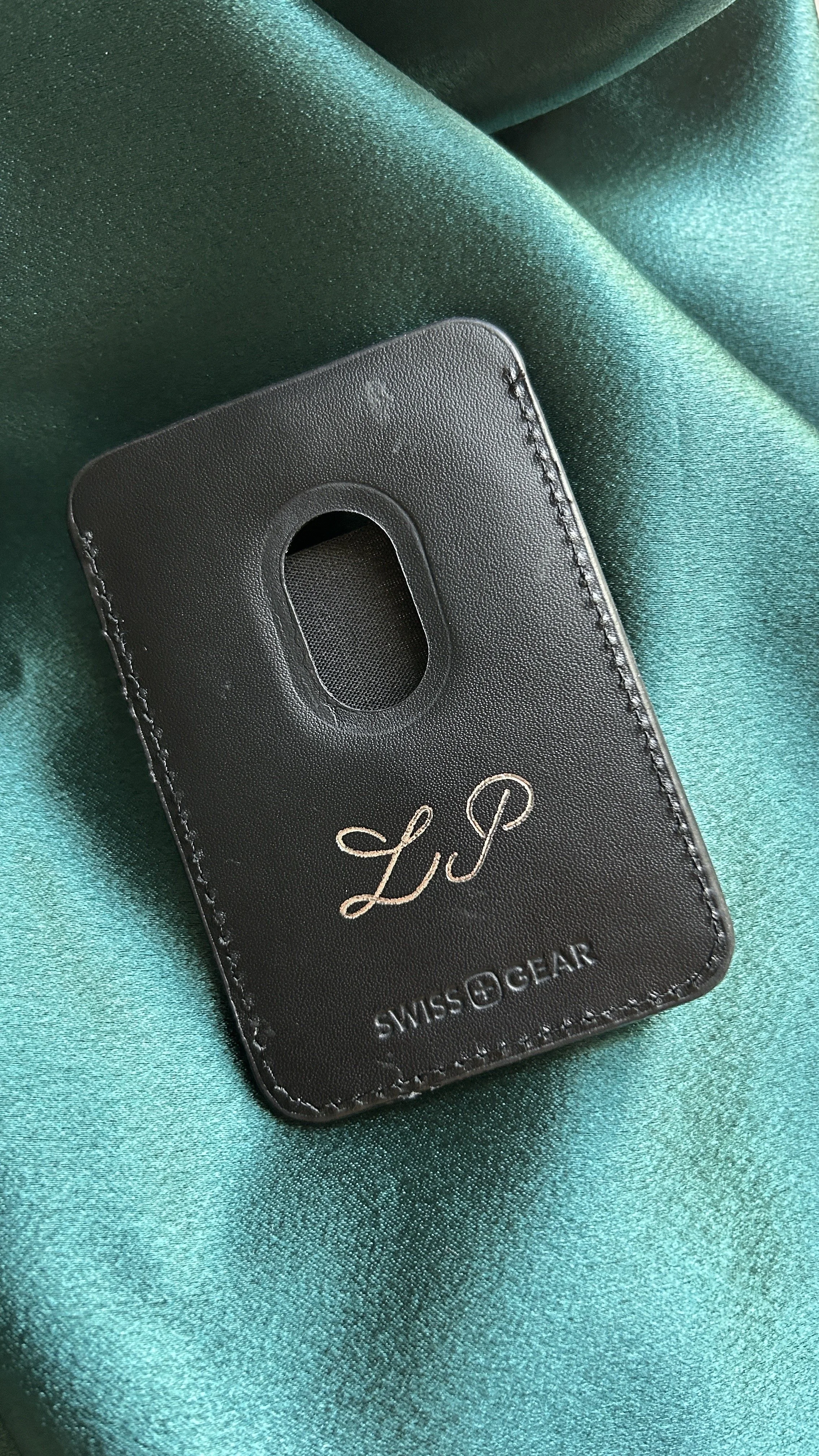 Black leather tag with a cutout window, engraved with the words 'LIP' and 'SWISS GEAR,' placed on shiny teal fabric.