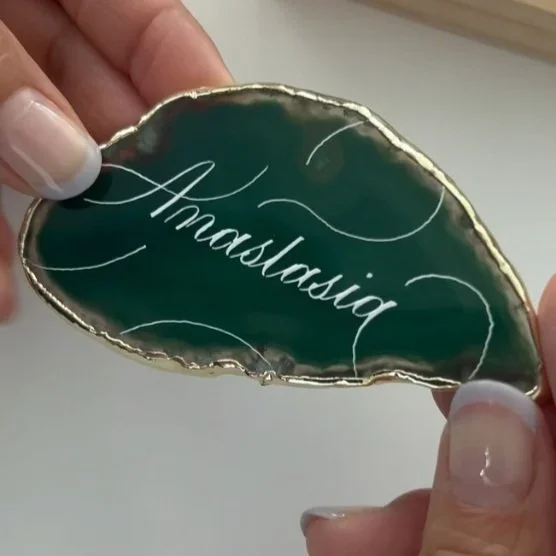 A person holding a green geode with gold edges and the word 'Amastasia' written in cursive in the center.