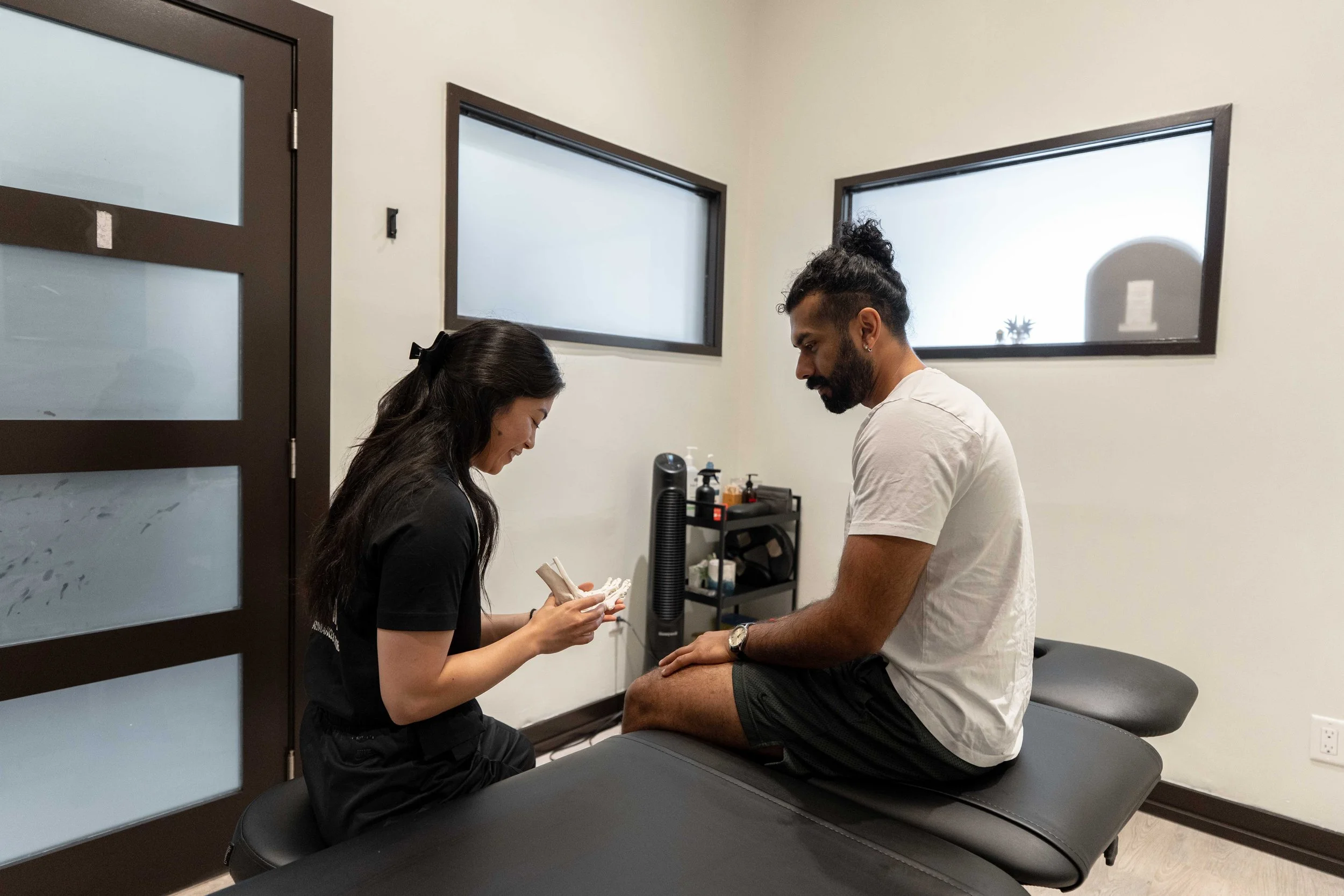 A chiropractor or physical therapist working on a male patient's knee in a clinic.