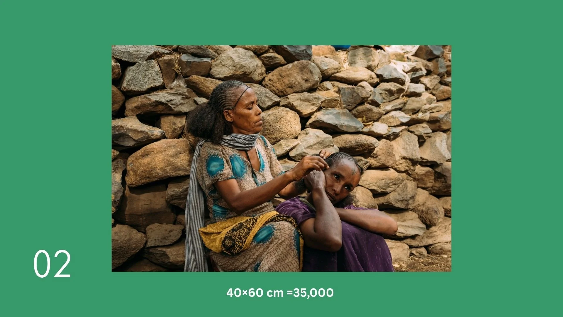 Two women, one older and one younger, sitting against a stone wall. The older woman is braiding the younger woman's hair.