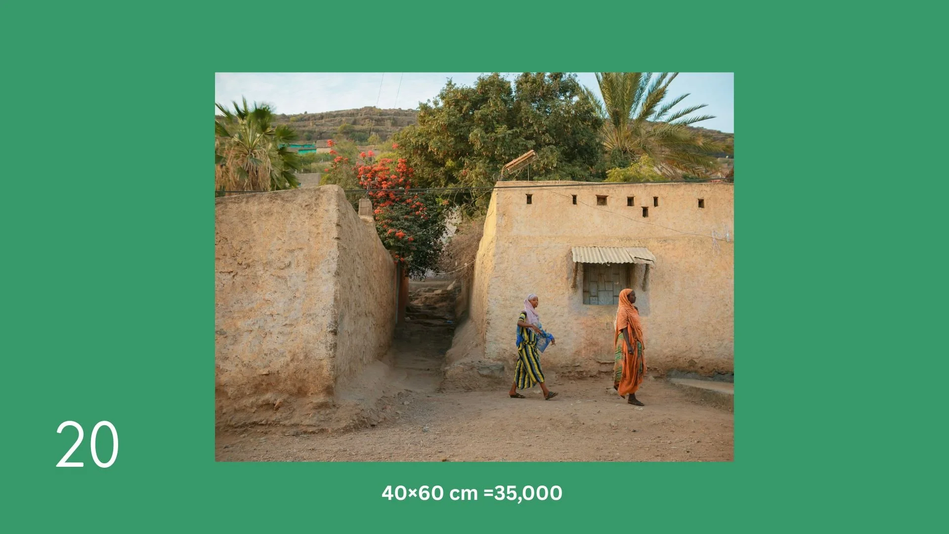 Two women walking past a mud-brick house with a small window and a corrugated metal awning, with trees and hills in the background.