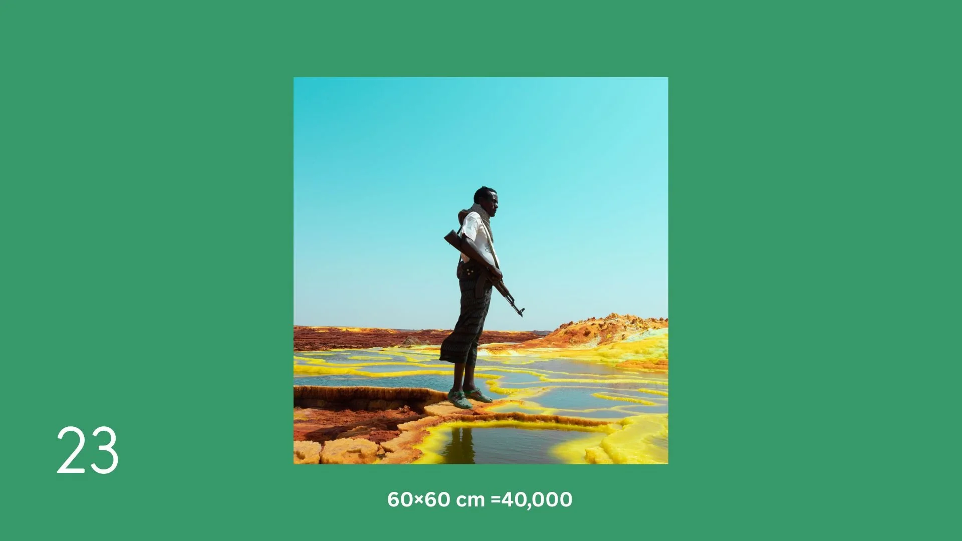 A man with a rifle standing on colored salt flats or mineral pools under a clear blue sky.