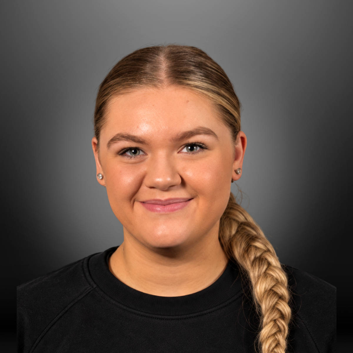 Close-up portrait of a young woman with blonde hair in a braid, smiling, wearing a black top, against a grey background.