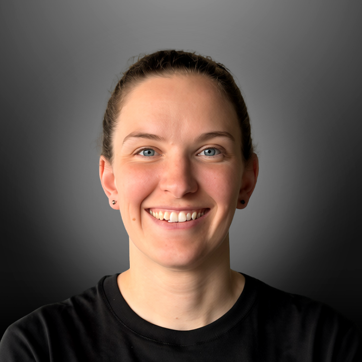 A young woman with light skin, blue eyes, dark hair pulled back, wearing a black shirt, smiling against a gray background.