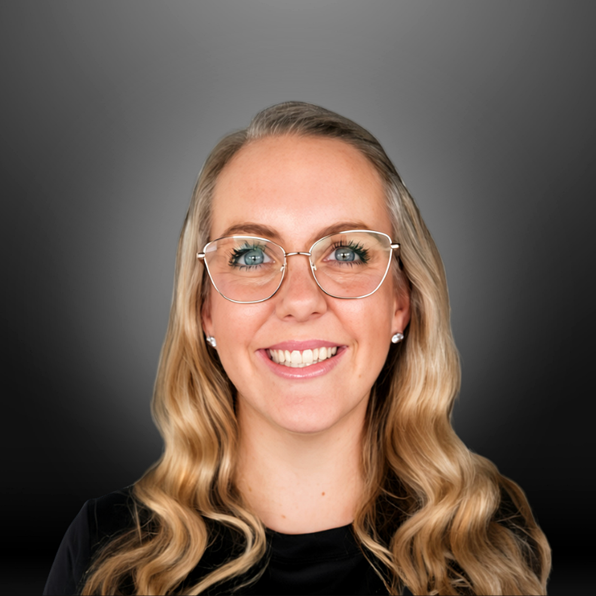 A woman with blonde wavy hair wearing glasses and earrings, smiling in front of a gray and black gradient background.