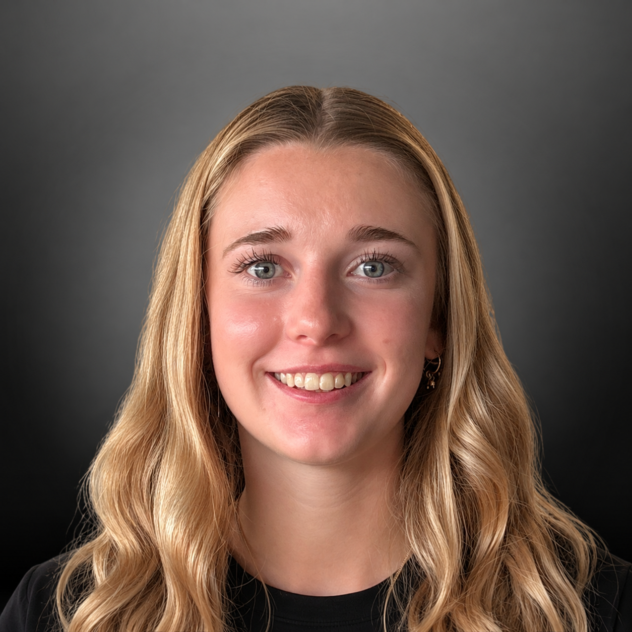 A young woman with long wavy blonde hair smiling at the camera against a dark gray background.