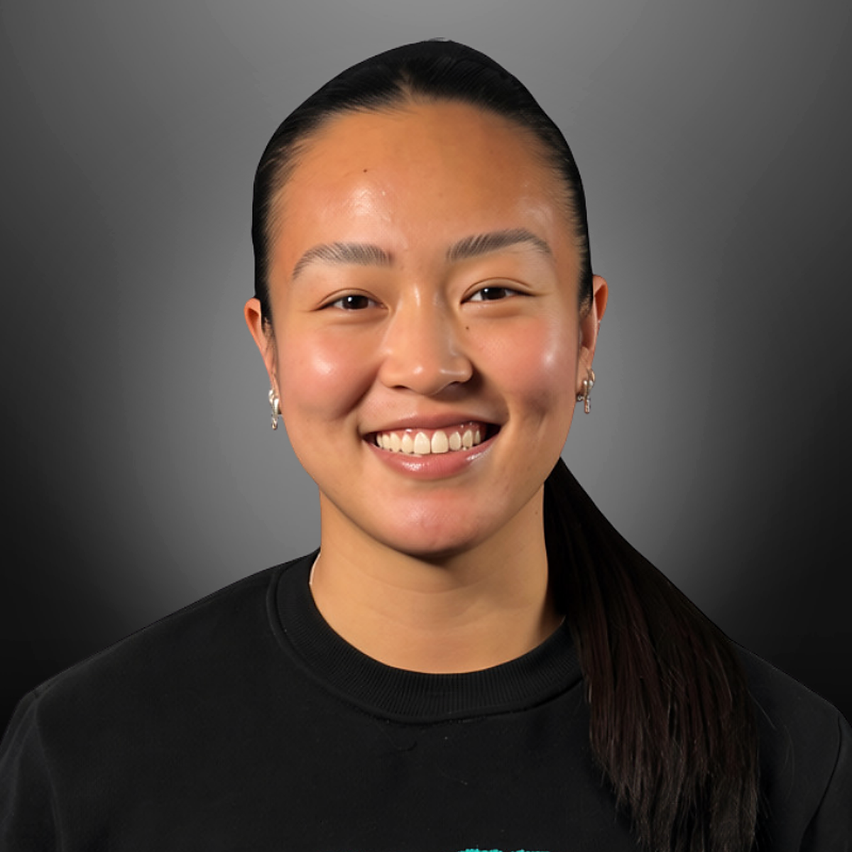 A young woman with dark hair pulled back, smiling, wearing earrings and a black shirt, against a gradient gray background.