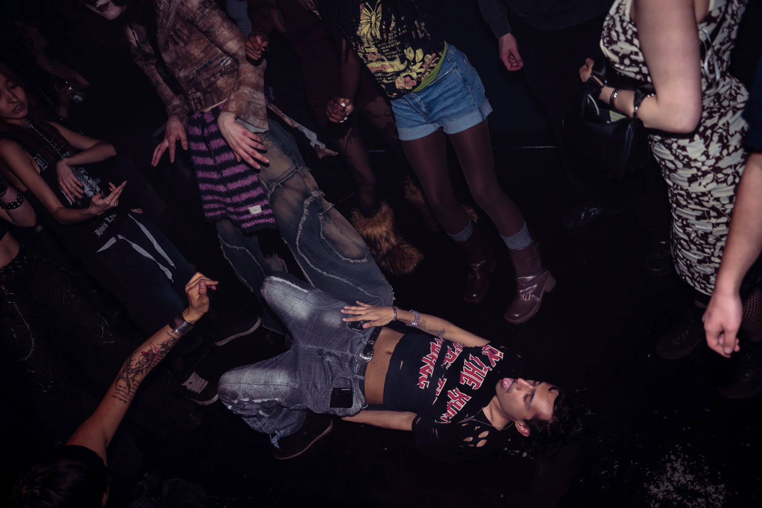 People at a music concert or event standing close together in a dark setting, wearing casual and alternative fashion.