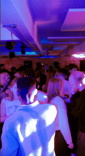 People dancing at a crowded party or club with purple and blue lighting.