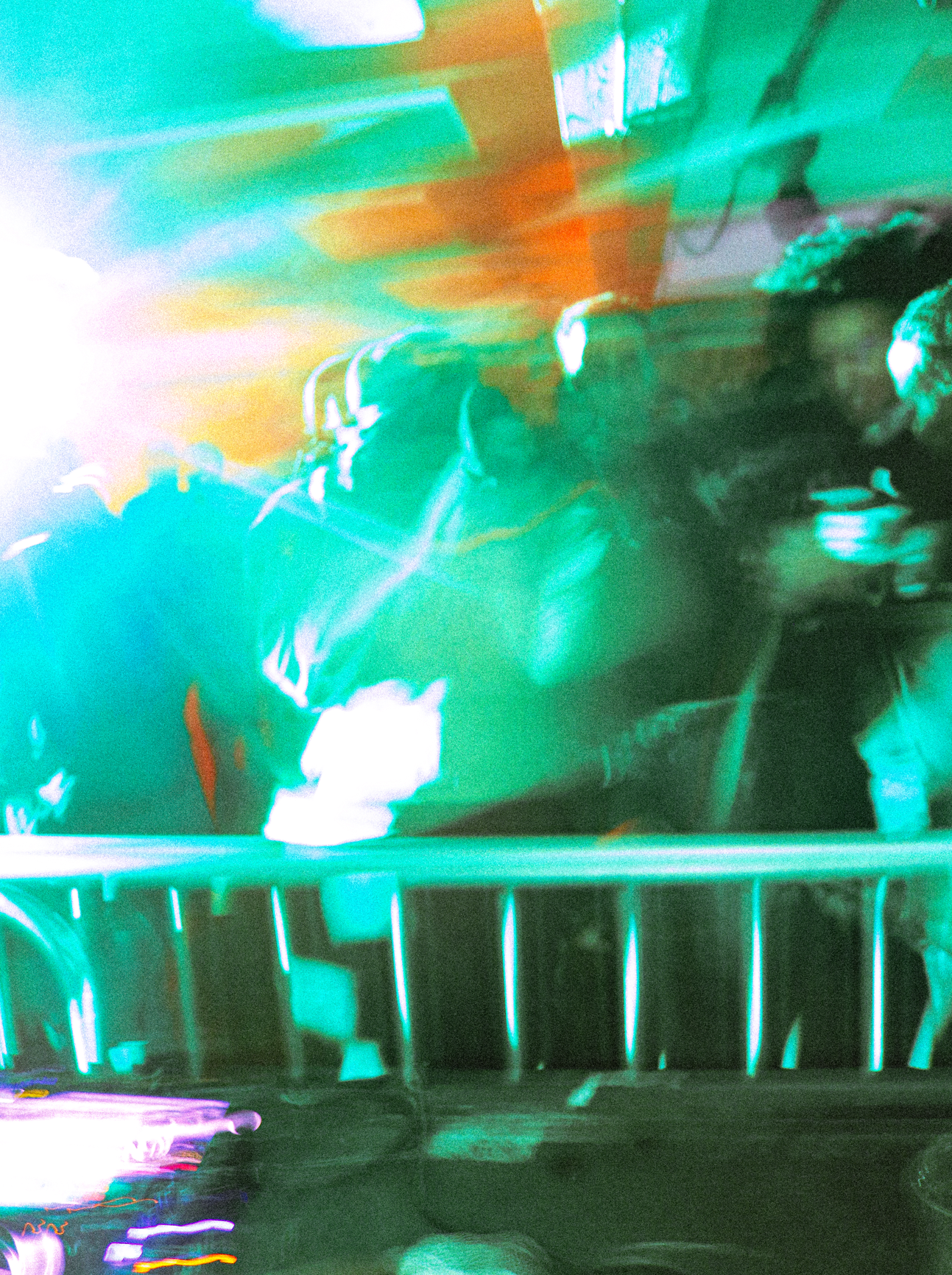 Colorful, distorted digital image of a person standing behind a railing, with neon lights creating abstract and blurred effects.