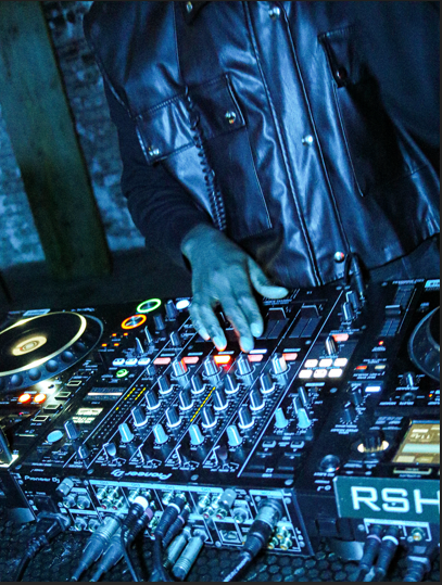 DJ mixing music on a professional DJ controller, wearing a black leather vest.