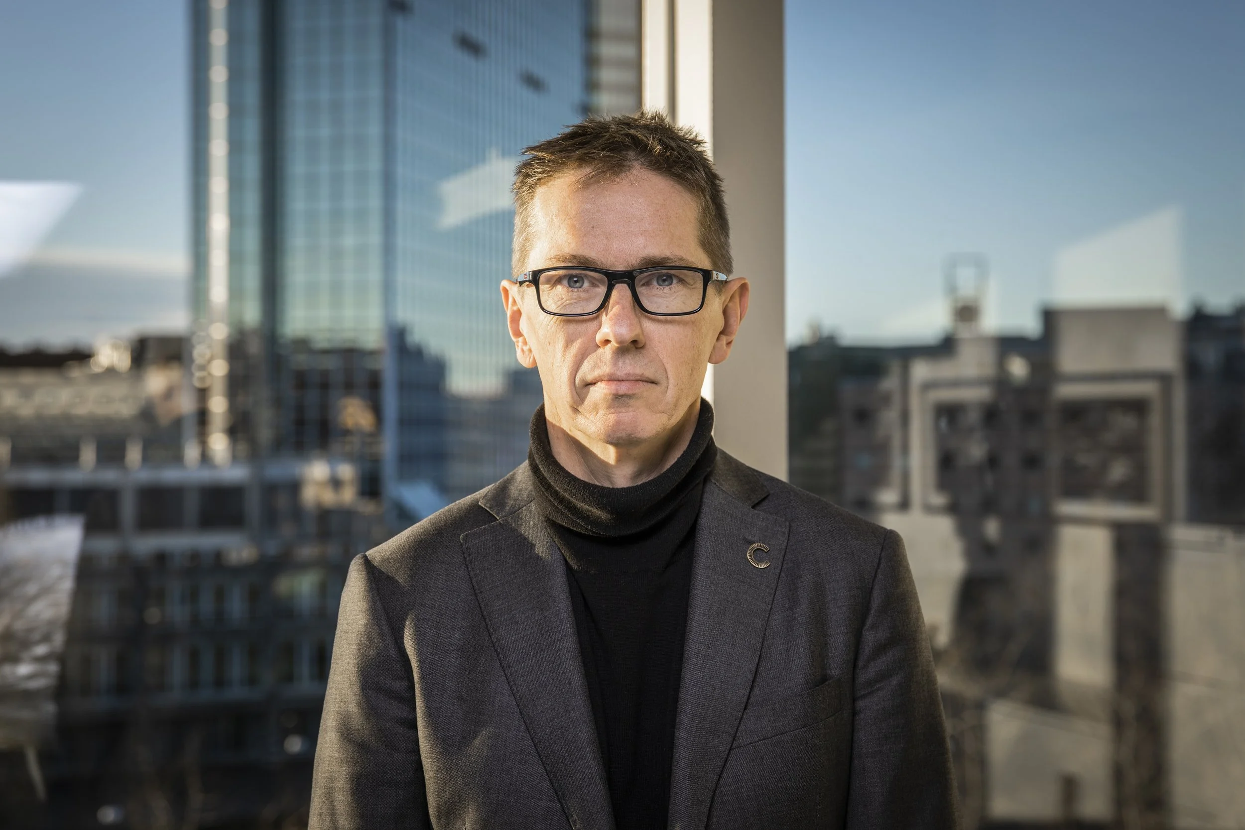 Forbundslederen Hans Ole Rian, avbildet med briller, mørk høyhalset genser og dressjakke, foran et høyt bygg i Oslo.
