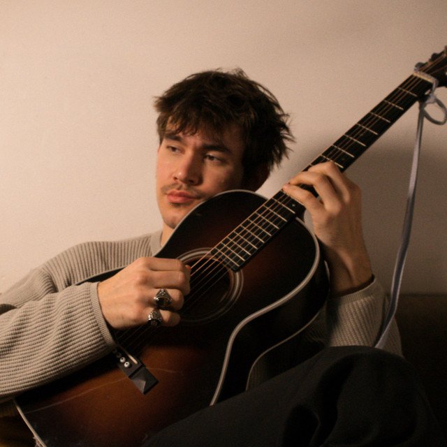 Jonge man speelt akoestische gitaar in een warme binnenruimte.
