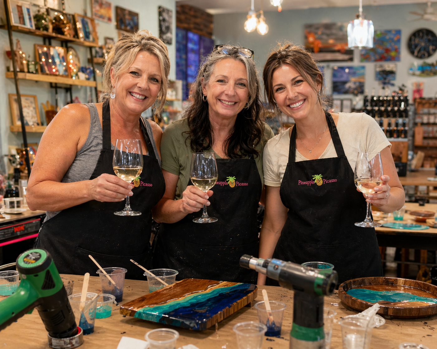 Women holding wine glasses during a paint and sip resin art event at Pineapple Picasso