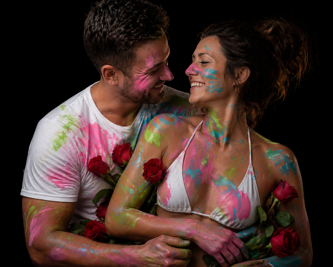 Couple covered in colorful paint and holding roses during a romantic Passion Prints couples art experience at Pineapple Picasso in Cape Coral, Florida.