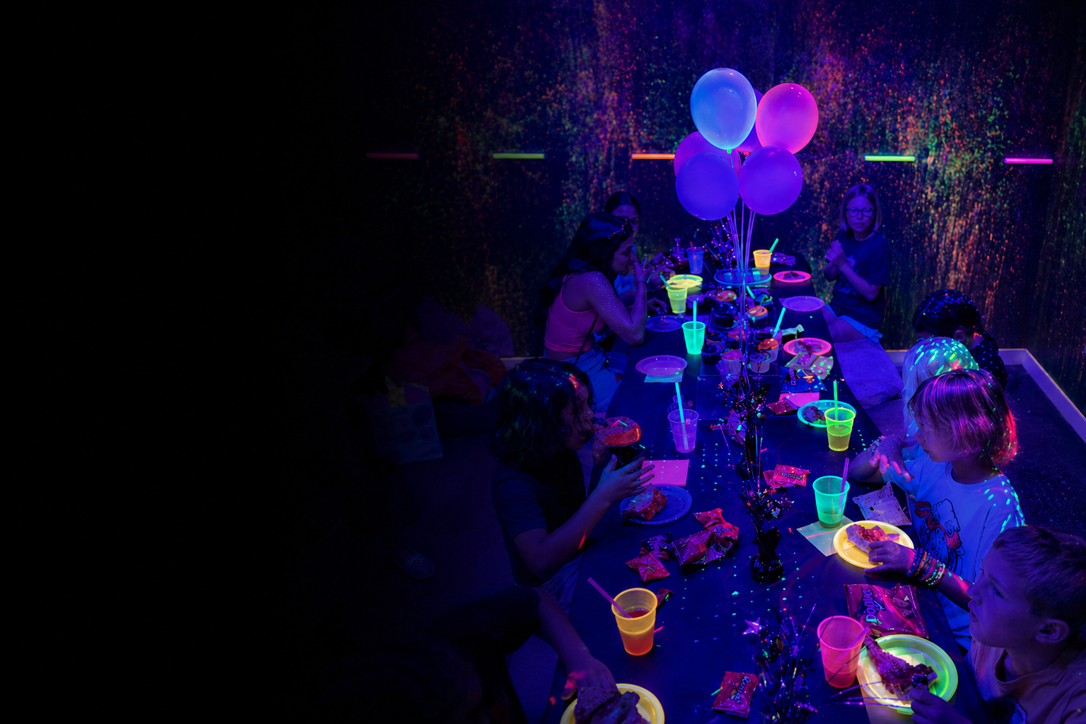Children celebrating a glow-in-the-dark birthday party with neon cups, balloons, and snacks