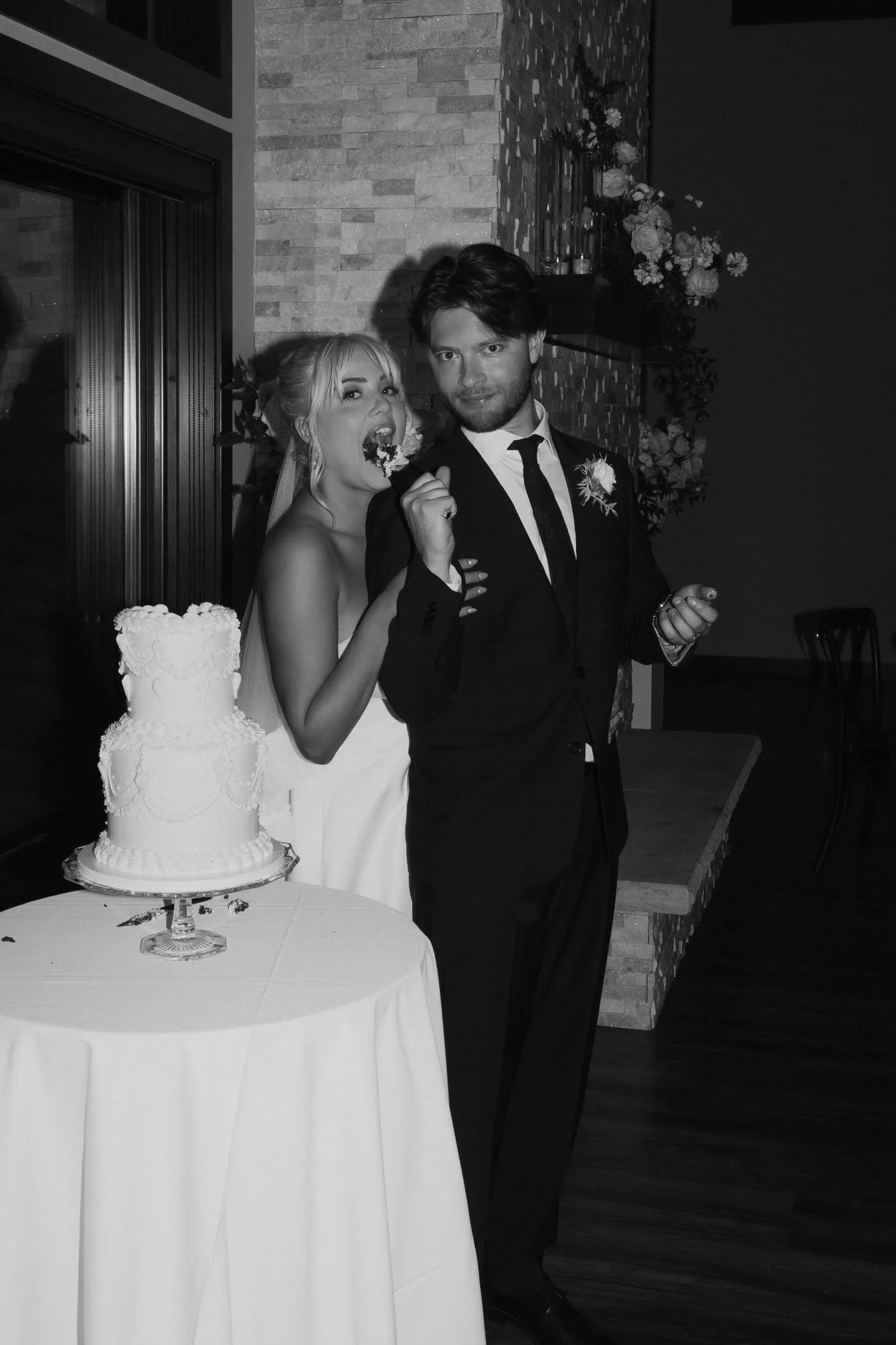 Groom feeds his bride a bite of their 2 tier vintage wedding cake.