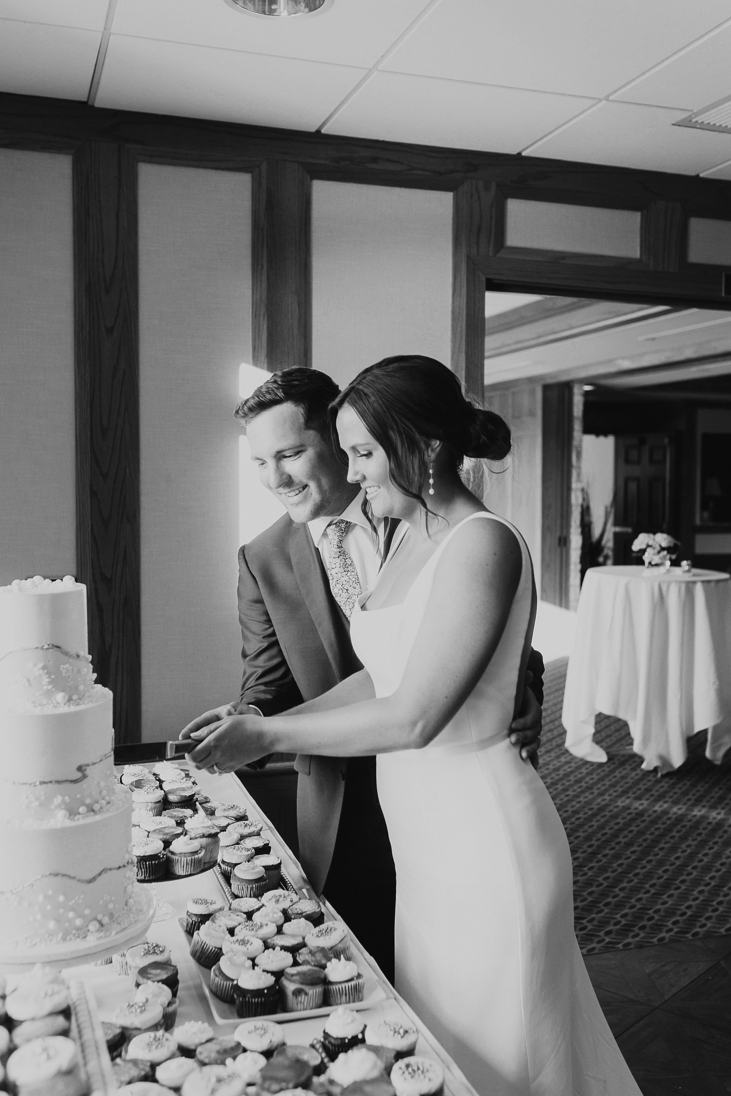 Happy couple cuts into their 3 tiered white and gold wedding cake.
