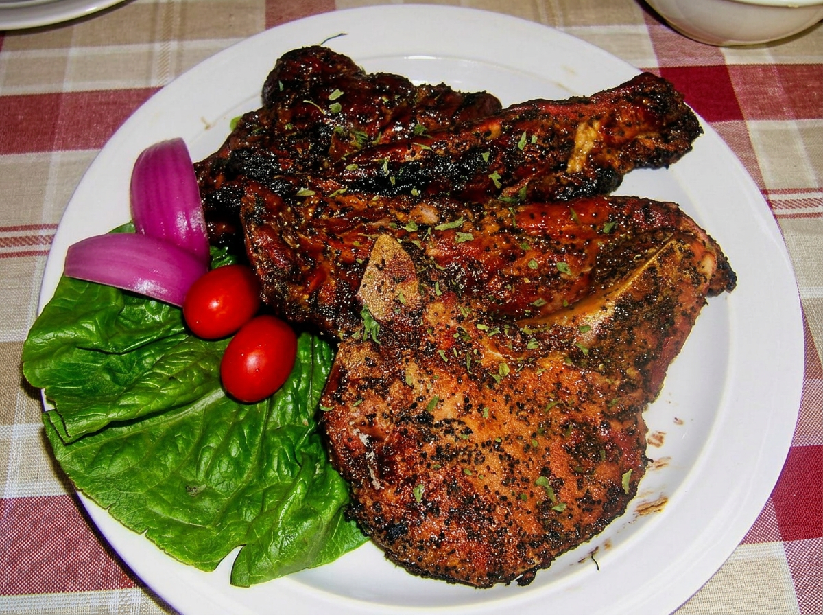 Grilled Pork Chops with lettuce leaf, served with cherry tomatoes, and sliced onions on a white plate.