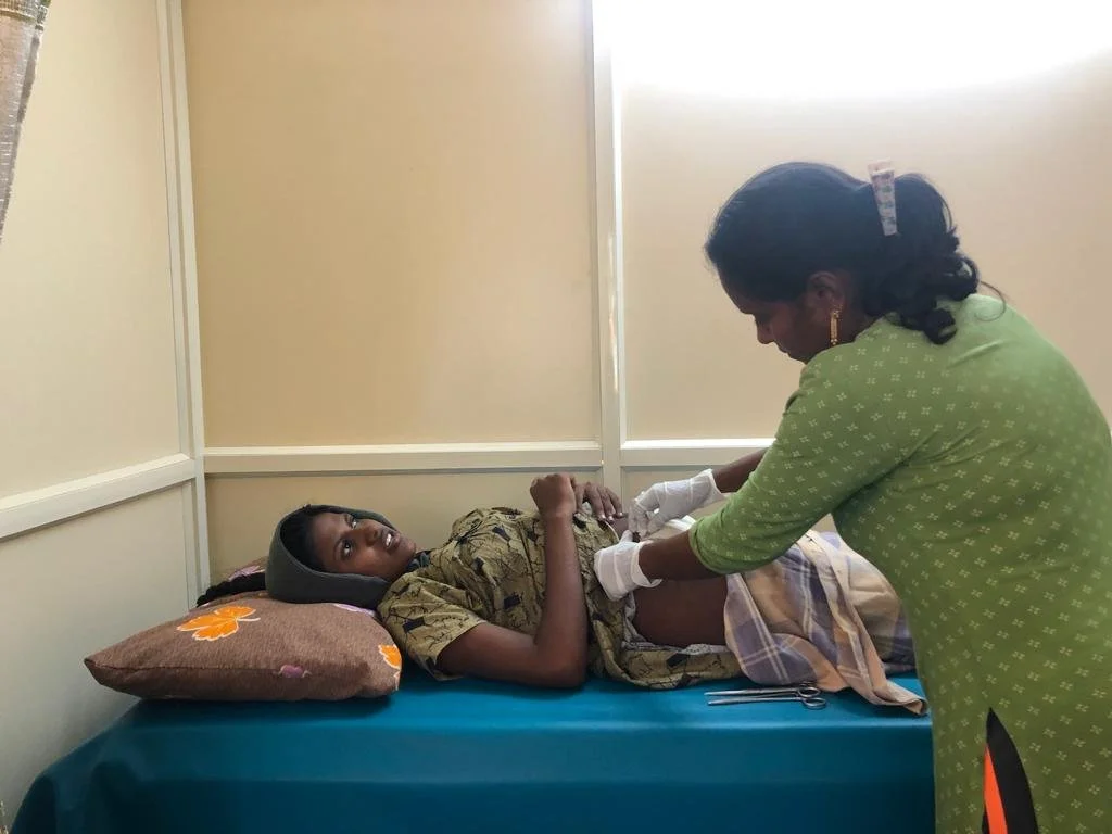 A woman lying on a hospital bed with a pillow under her head, while a nurse or healthcare worker examines her abdomen.
