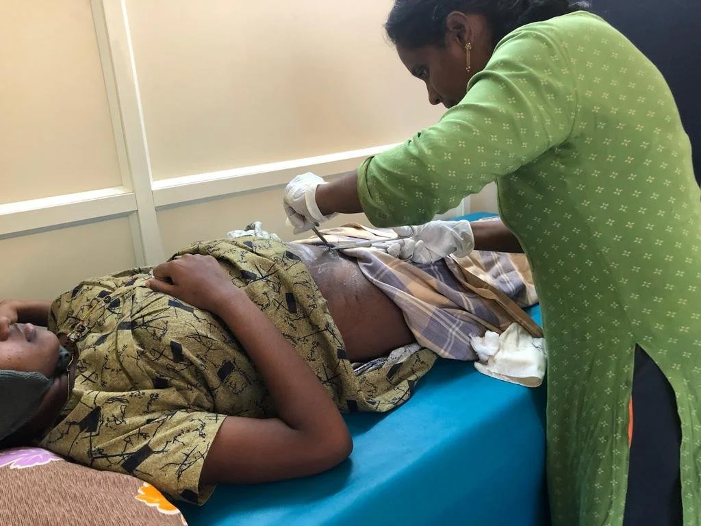 A healthcare worker in a green outfit administering an injection to a patient lying on a hospital bed.