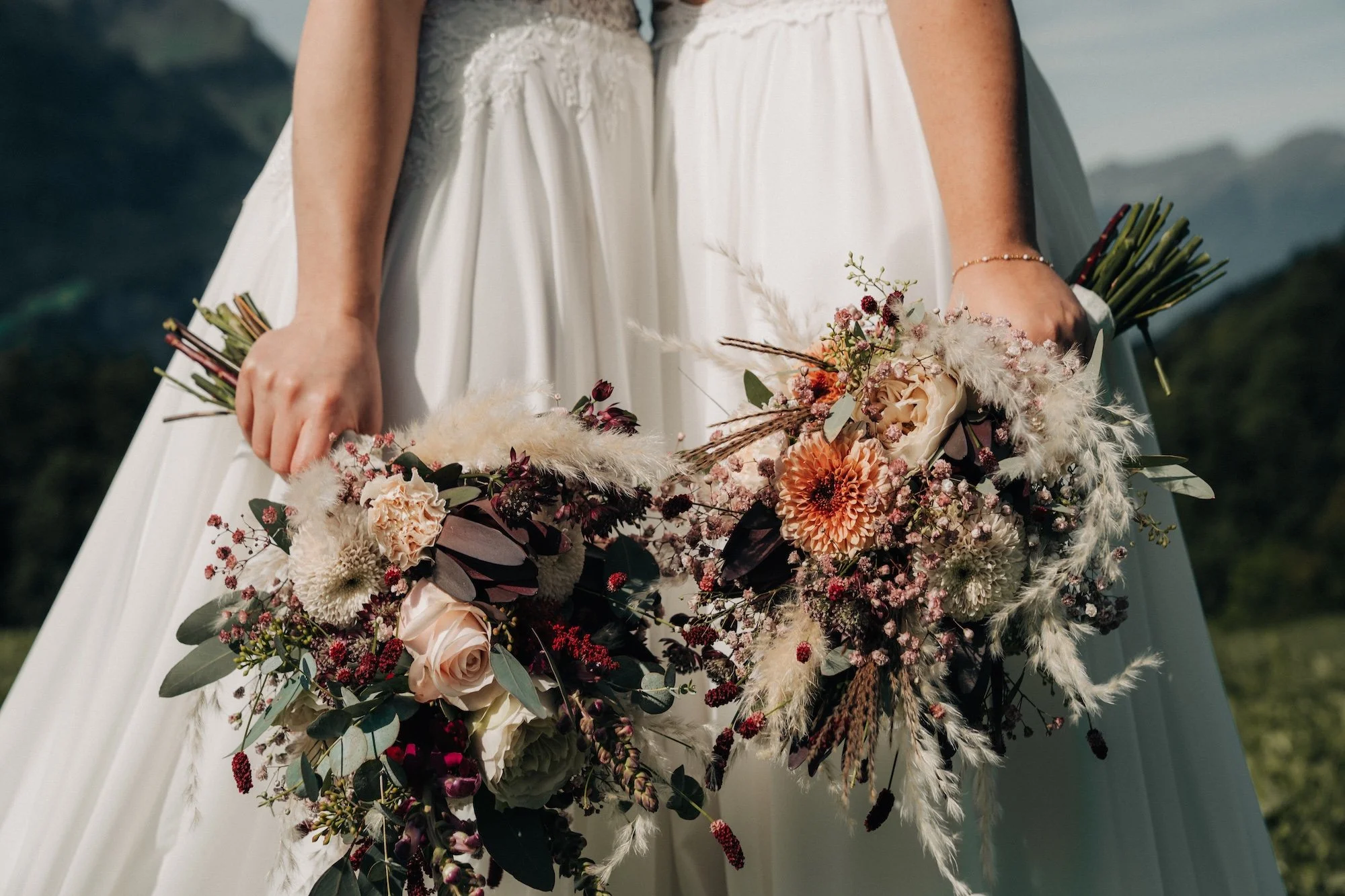 Hochzeitsfotografie für LGBTQ-Paare in der Schweiz – zwei liebevoll gebundene Brautsträusse vor weissen Hochzeitskleidern.