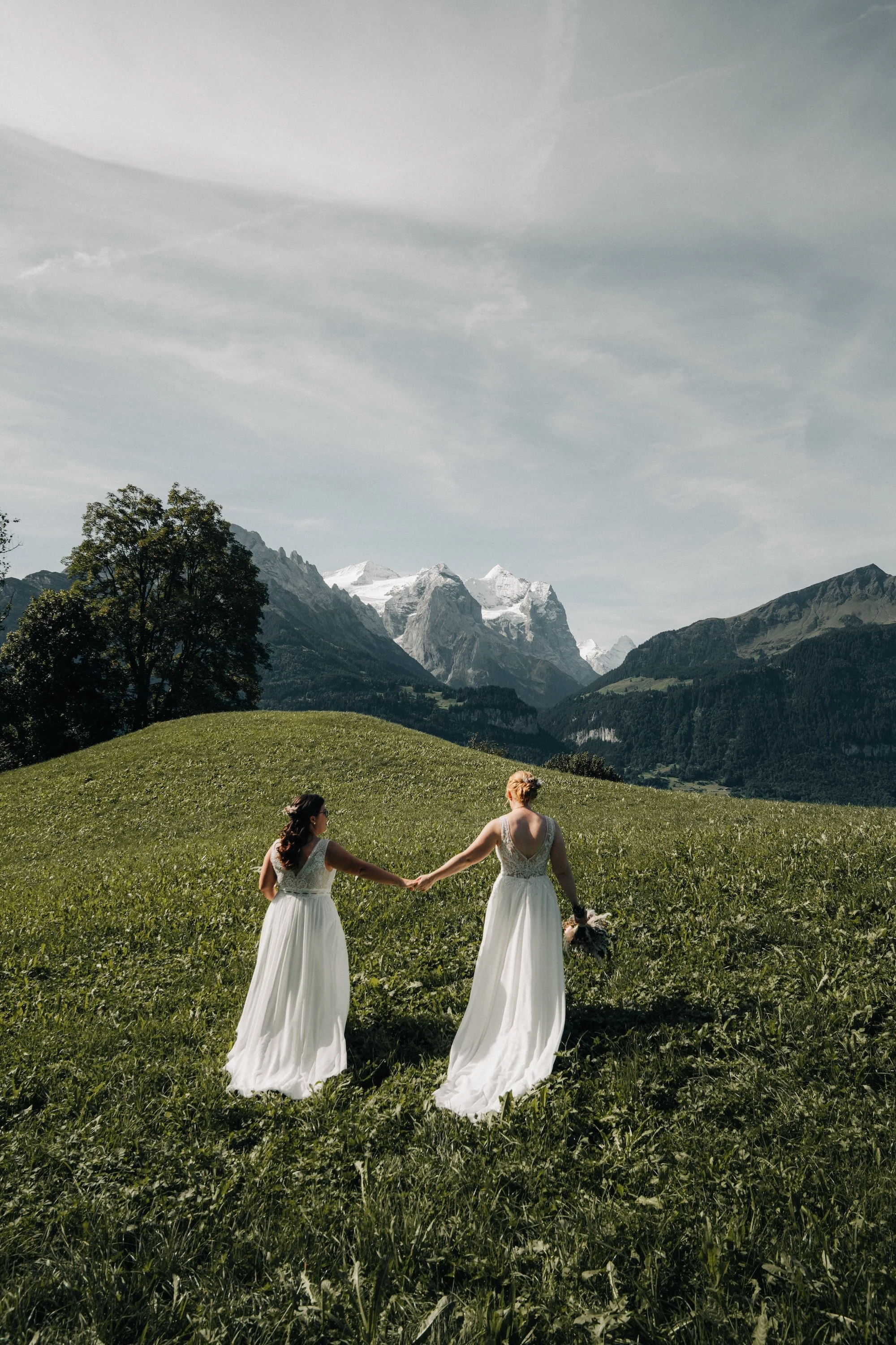 Hand in Hand durch die Bergwiese: LGBTQ-Hochzeit mit Blick auf die Berge des Berner Oberlands.