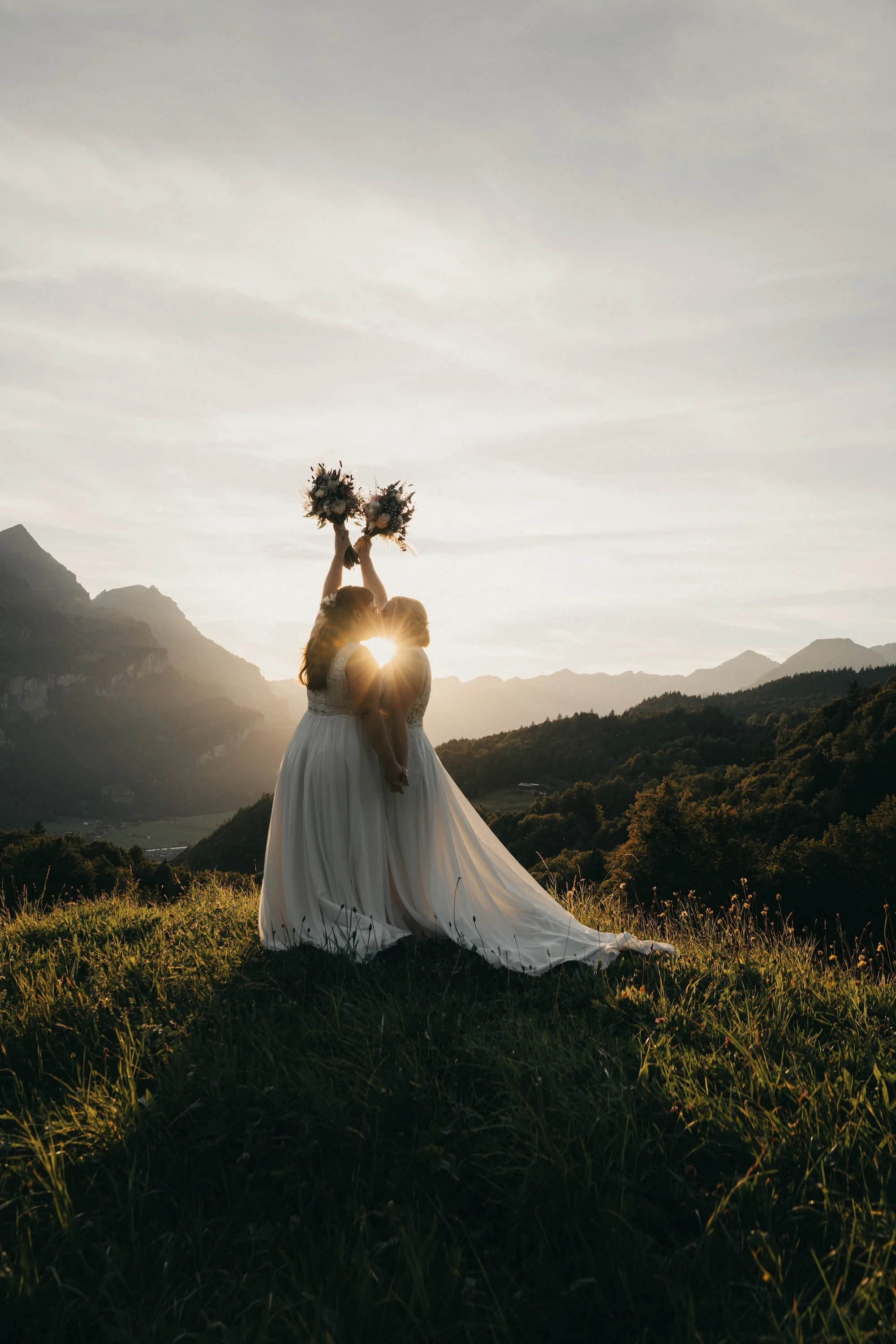 Zwei Bräute, zwei Brautsträusse und die Abendsonne über den Bergen – LGBTQ-Hochzeit in der Schweiz.