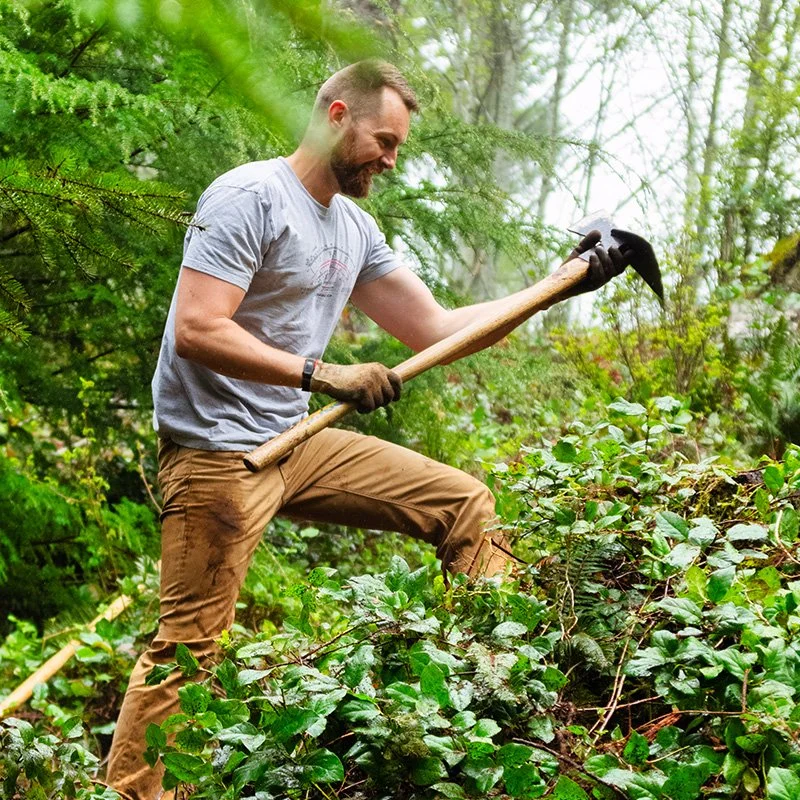 man building mountain bike trail, viewed through trees