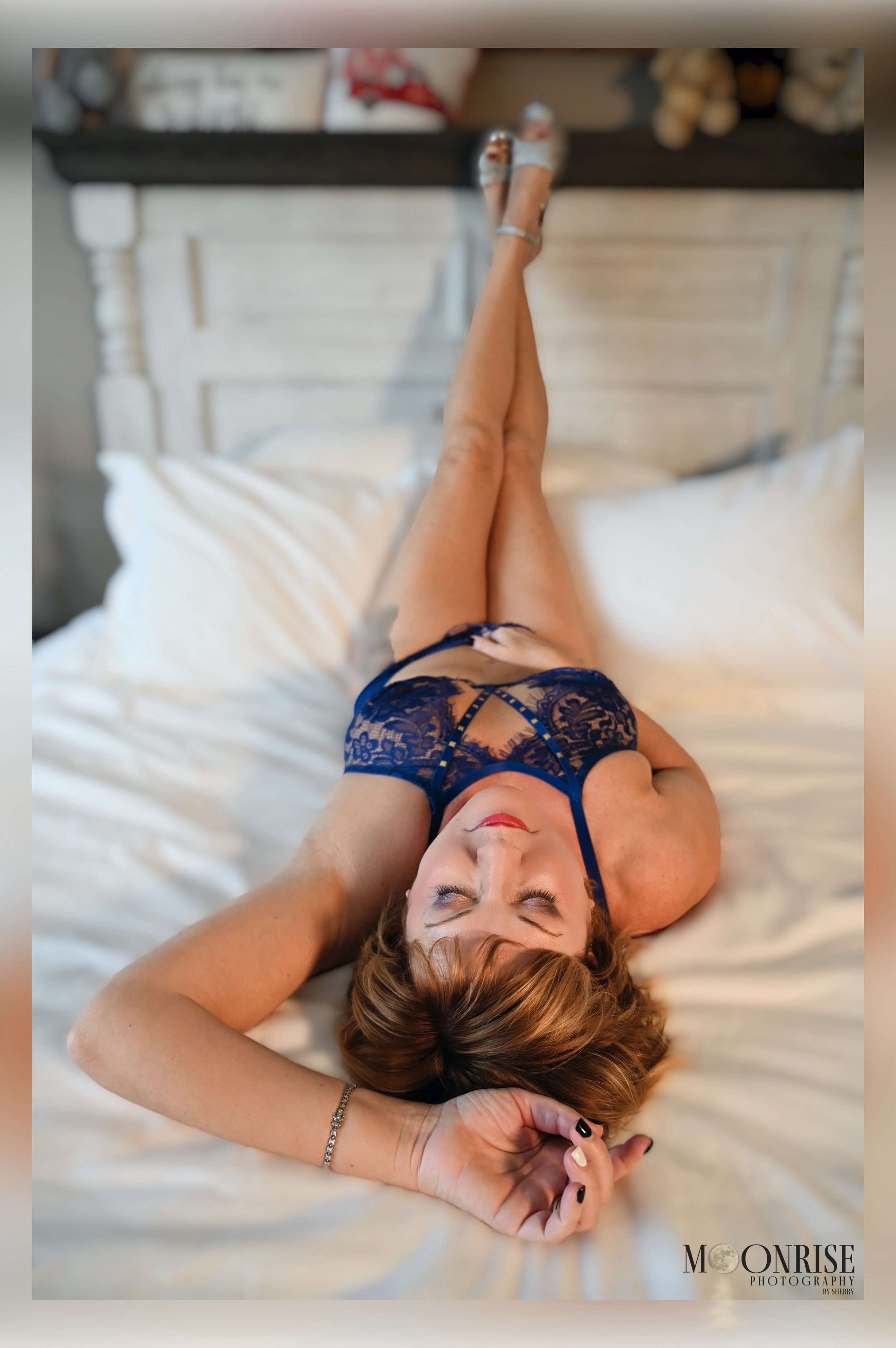Woman relaxing on bed in blue lingerie with heels, eyes closed.