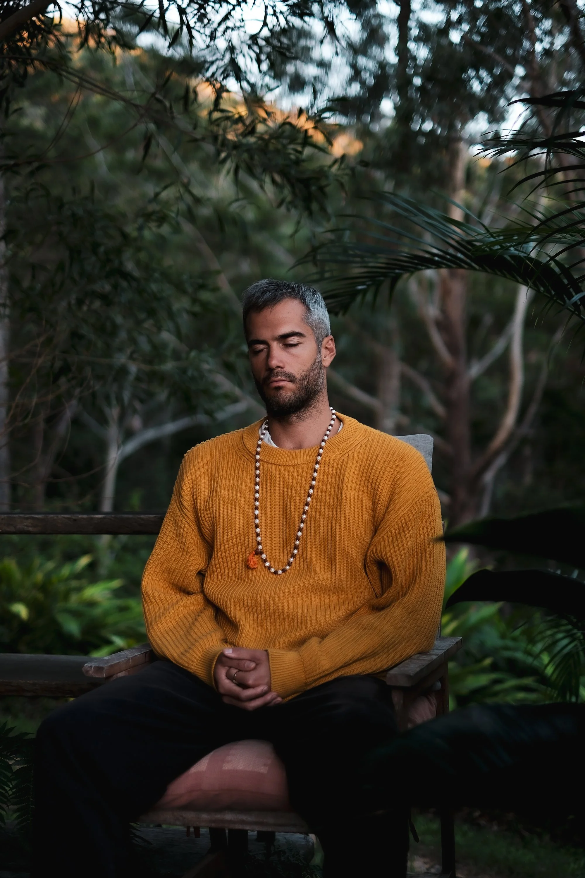 Man in a mustard jumper meditating in the bush