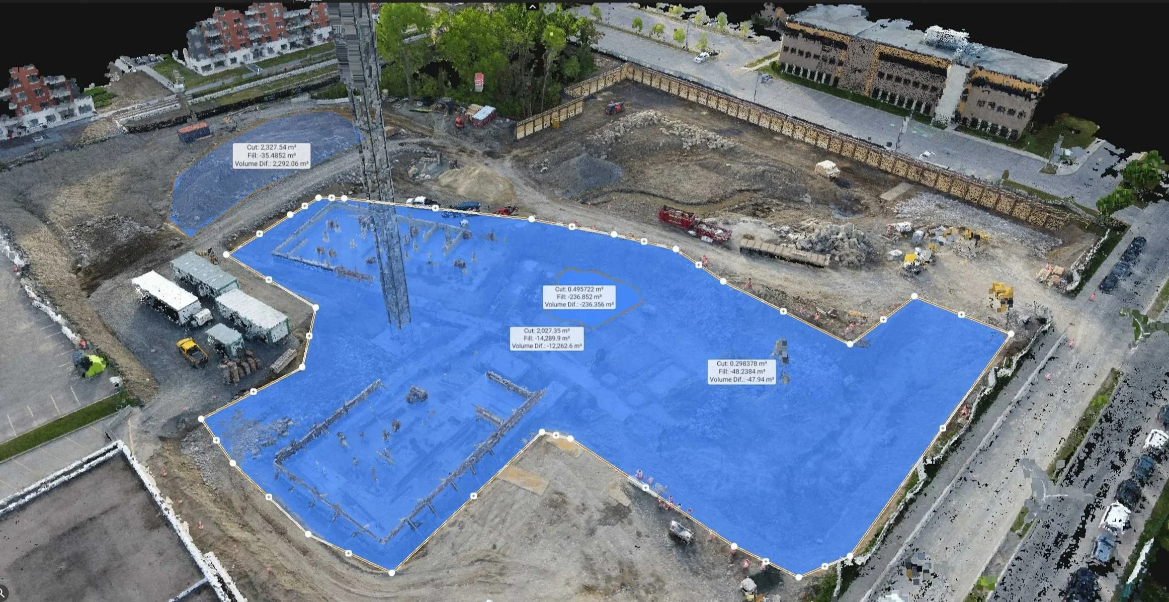 Aerial view of a construction site with the mapping area highlighted in blue, showing measurements and volume differences, with surrounding buildings, vehicles, and greenery.