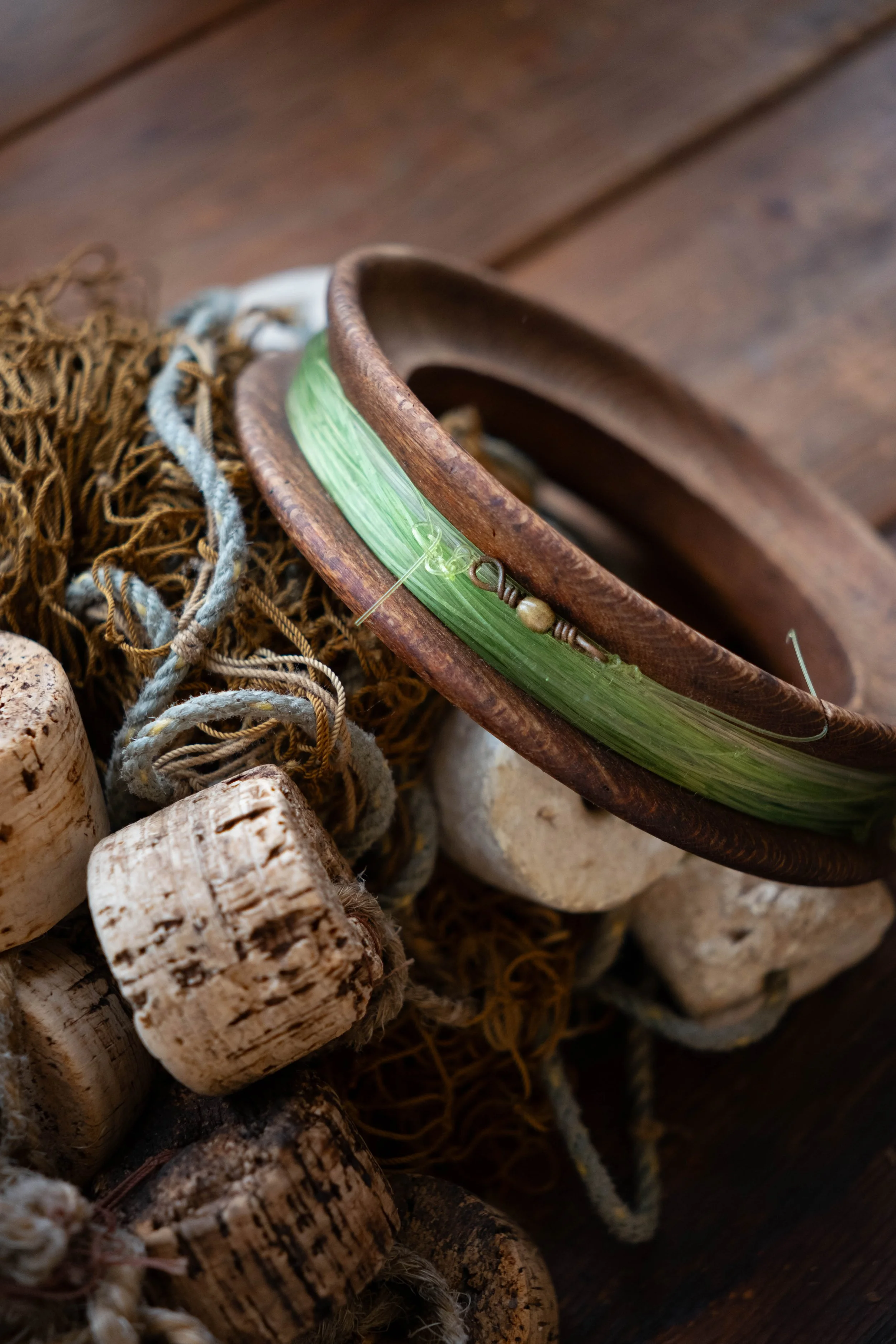 Close-up of a wooden bowl with a green glass art decor, surrounded by corks, ropes, and a rustic wooden surface.