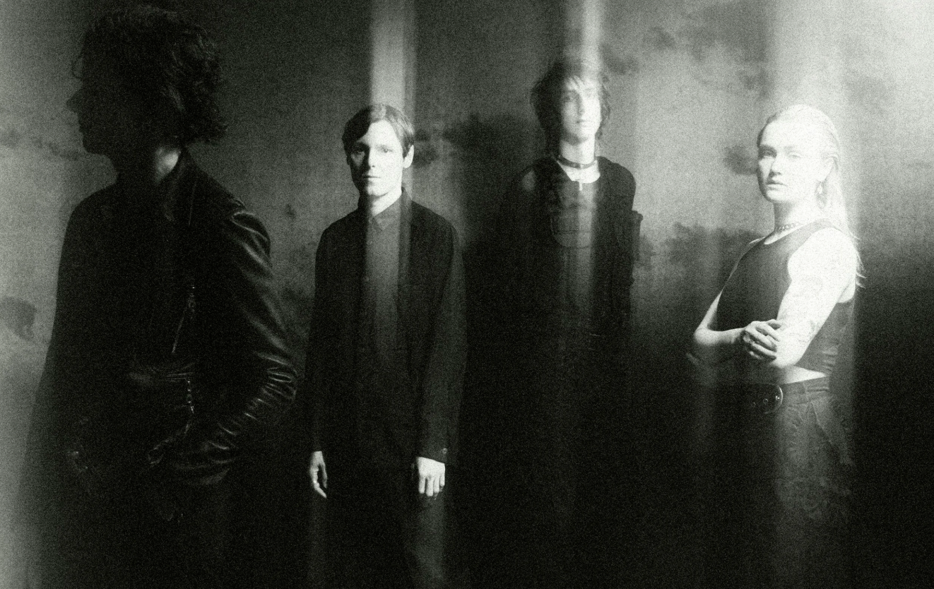 The Horrors band members in a moody, black and white grain-filtered press photo. Four musicians posing in dark clothing with ethereal light leaks.