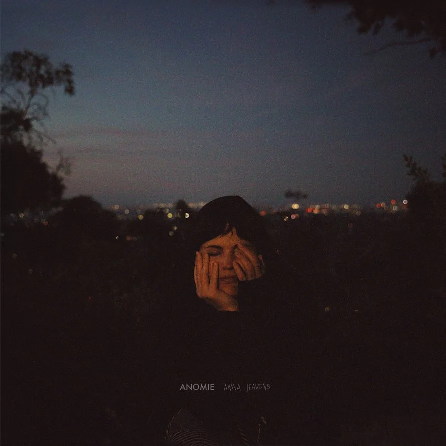 Indie artist Anna Jeavons in a moody night portrait by Mariah Anzil. A grainy, low-light shot with city lights bokeh and a dark, atmospheric feel.