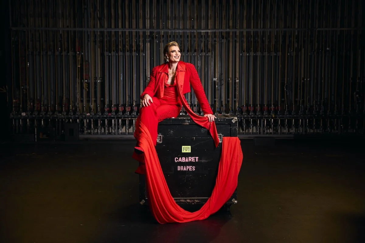Adelaide Cabaret Festival Artistic Director Reuben Kaye in a striking red outfit, sitting on a theater road case backstage. Photo by Claudio Raschella.