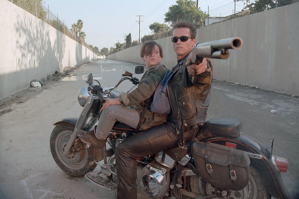 Arnold Schwarzenegger as the T-800 on a motorcycle with John Connor, aiming a shotgun in the Los Angeles drainage canal in Terminator 2: Judgment Day.