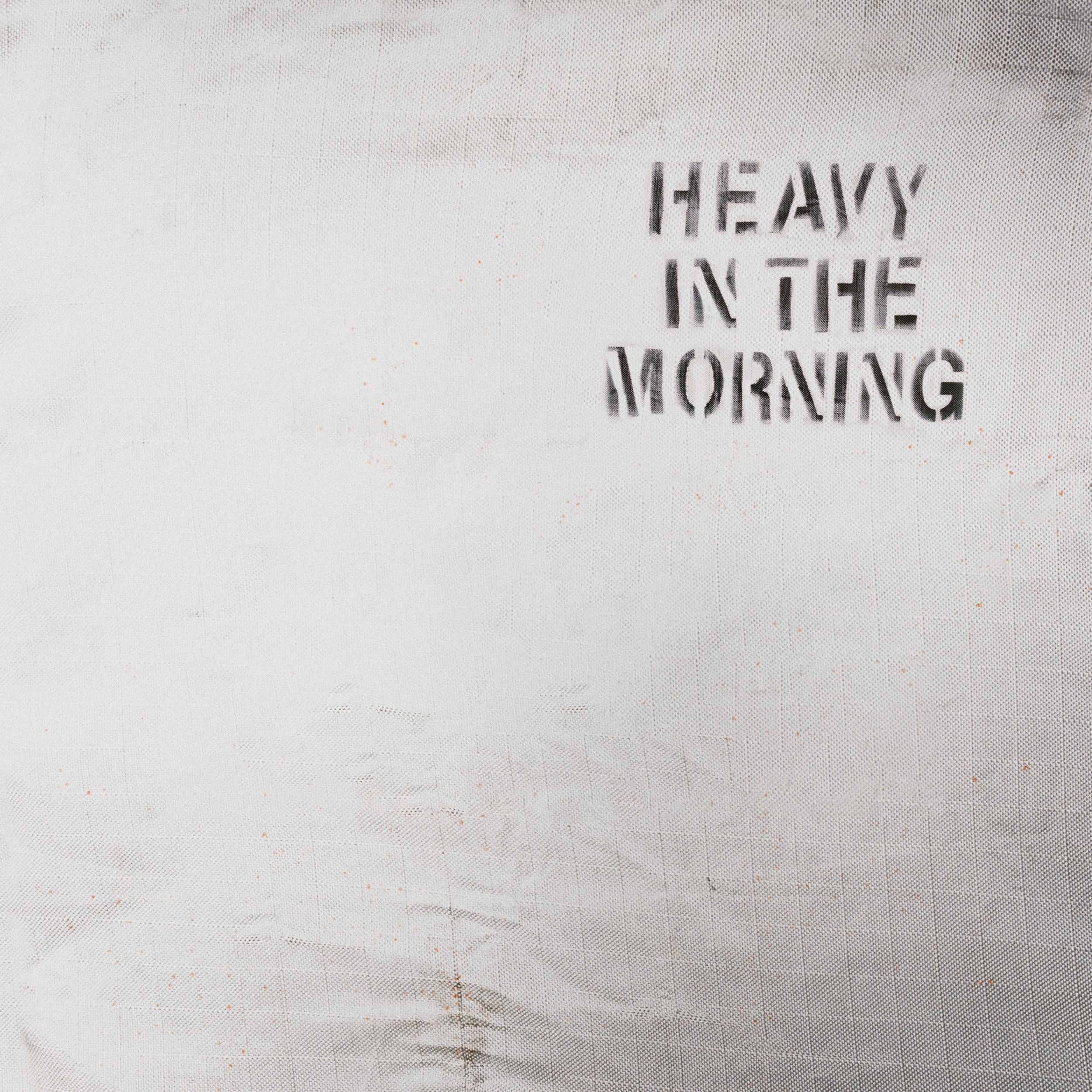 Minimalist artwork for Old Mervs' single "Heavy In The Morning." Stenciled black text on a textured, off-white fabric or industrial tarp background.