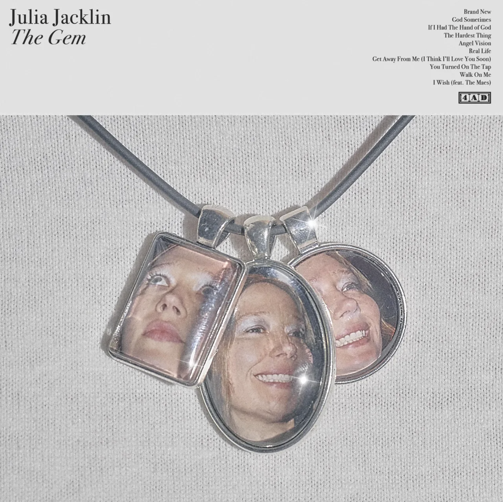 Album artwork for Julia Jacklin's "The Gem," showing a black cord necklace with three silver pendants featuring her face over a white textured background.