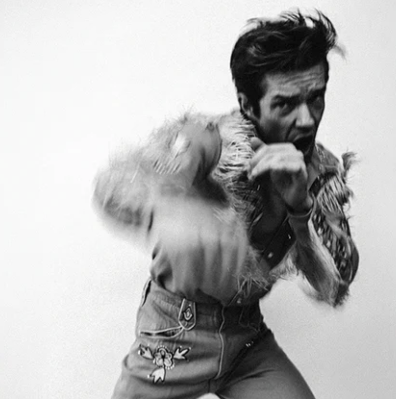 Black and white photo of Brandon Flowers throwing a blurry punch, wearing a fringed western shirt and embroidered pants for Thrasher album artwork.
