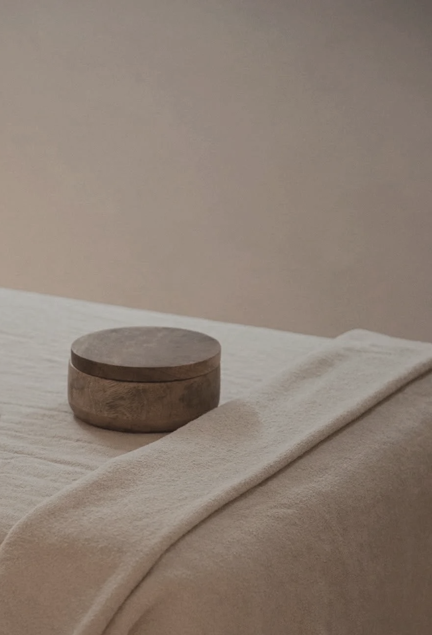 Carefully dressed massage table with white cotton sheets, ivory linen blanket, and ceramic container of essential oils for relaxation massage services