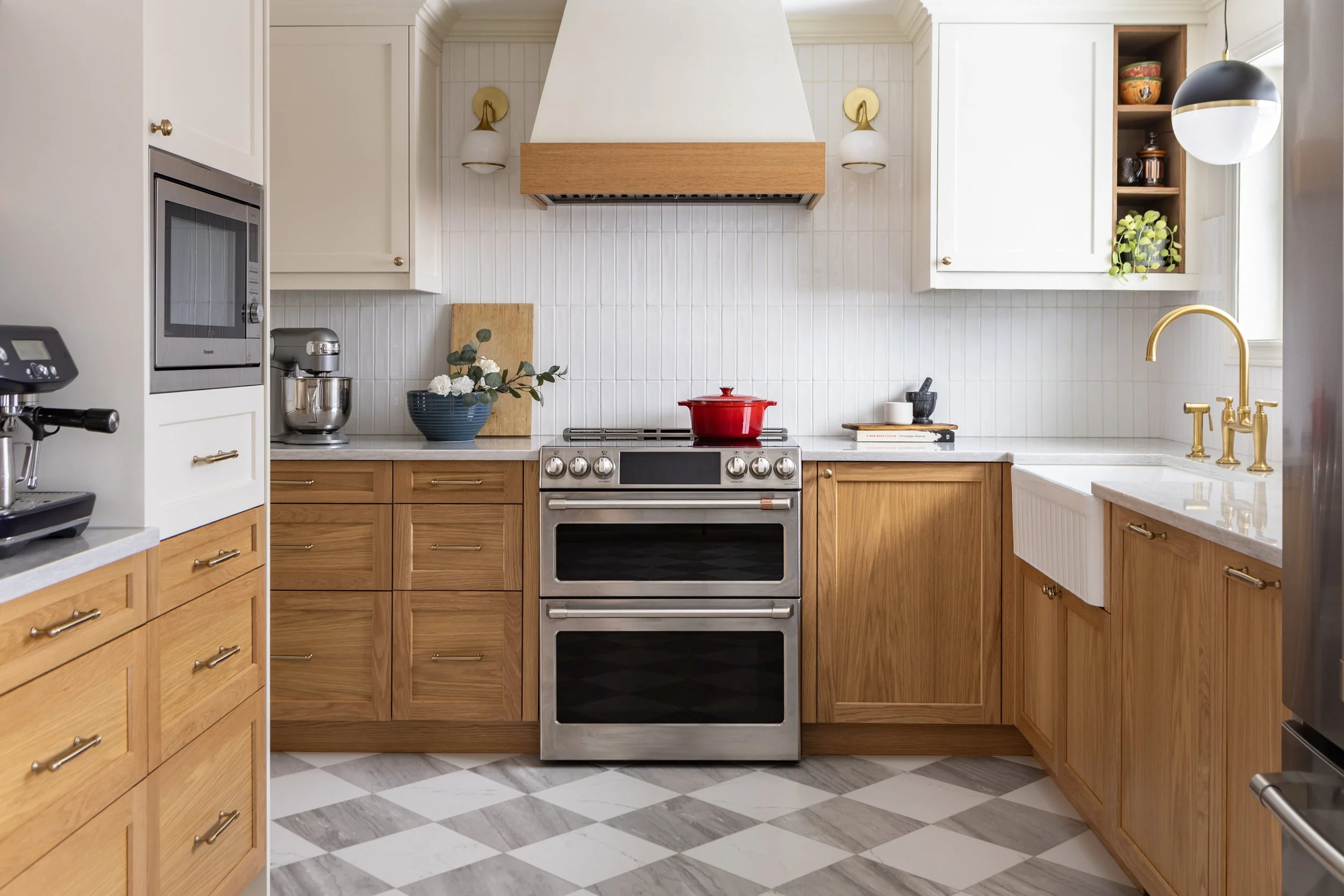 Moody transitional kitchen renovation in Ajax Ontario featuring two-tone cabinetry with white oak lowers and painted white uppers, brass hardware, custom range hood, and black fixtures by Inspired Spaces Design Studio