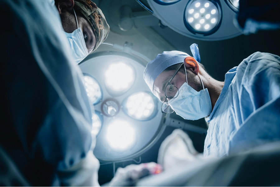 View from the patient on the operating table, of  2 male surgeons in masks and scrubs. Bright light above.