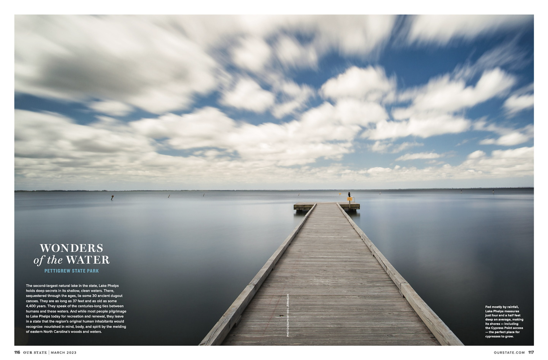 Long exposure photograph of a wooden pier extending into Lake Phelps under a partly cloudy sky.