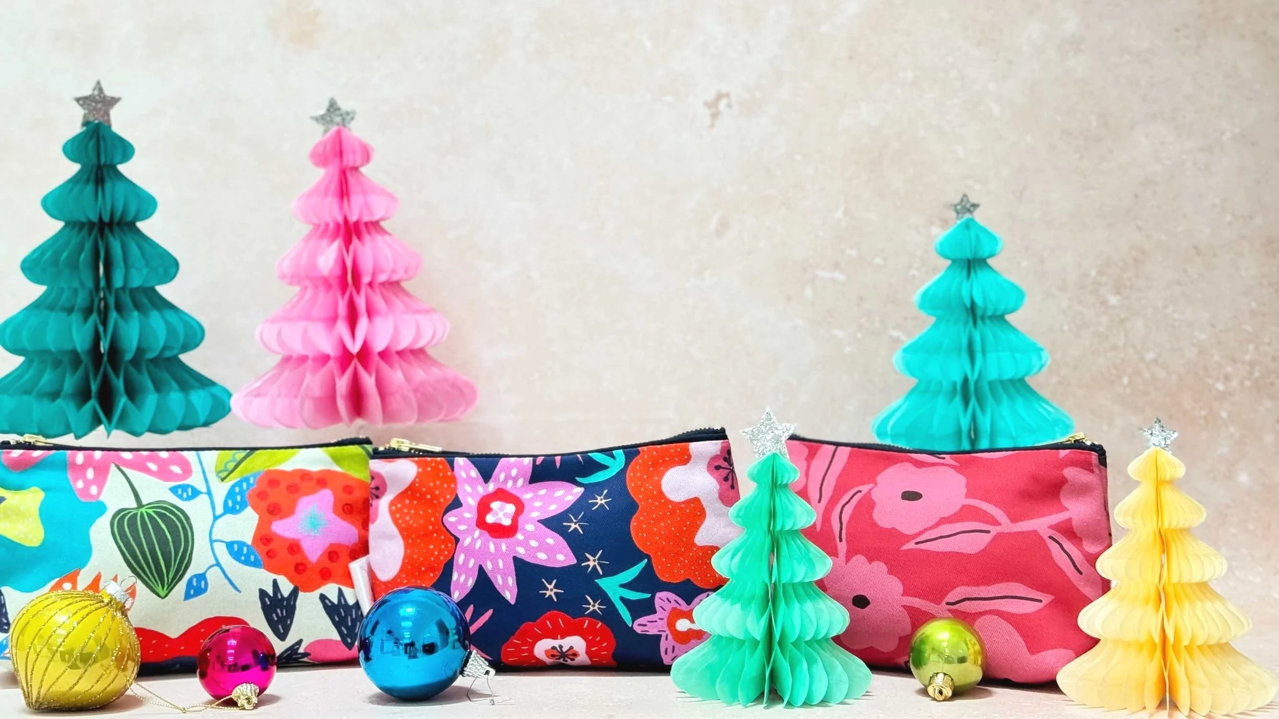 Bold patterned multicoloured small makeup bags made in the UK by Jennie Fynn with Christmas baubles and paper Christmas trees