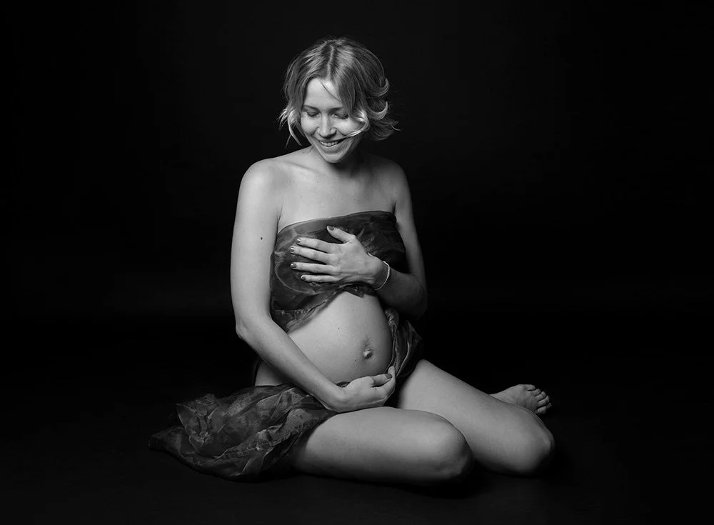 Gravidfoto sittandes svart-vitt mörk bakgrund studio