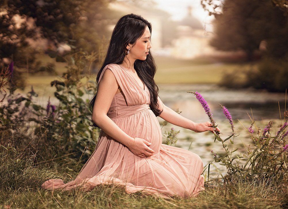 Gravidfotografering ute natur sittandes i gräs med blommor