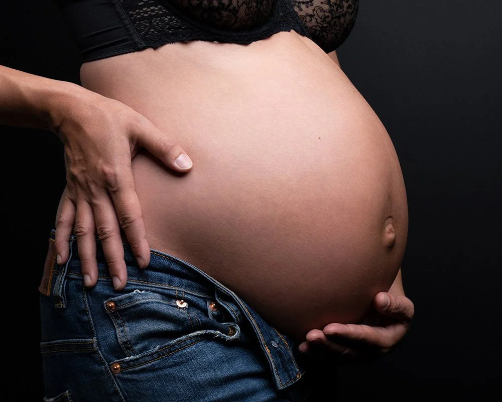 Gravidfoto i jeans och bh med svart bakgrund fotostudio