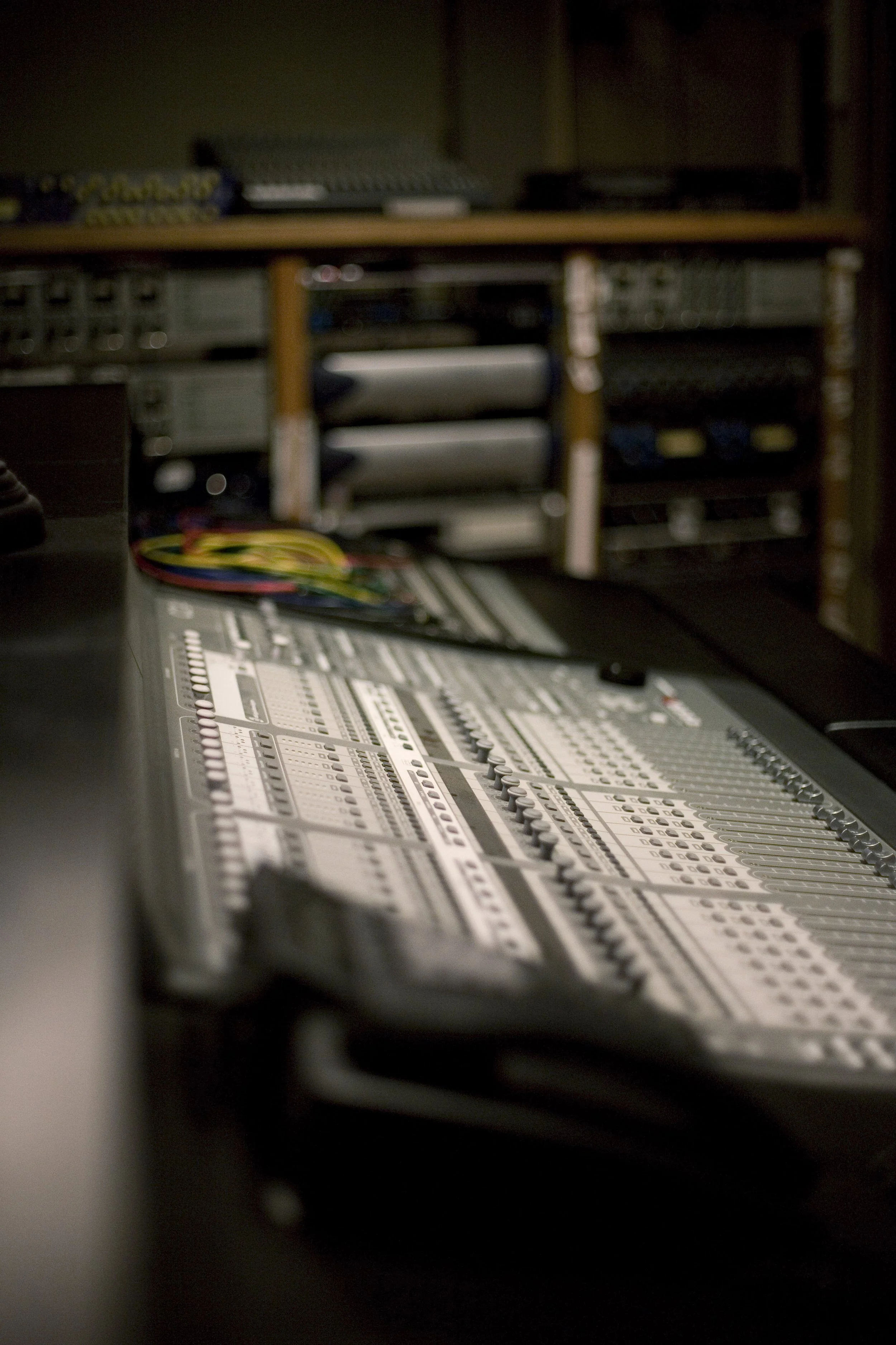 A professional audio mixing console with numerous knobs, sliders, and colorful cables in LLMG recording Studio A