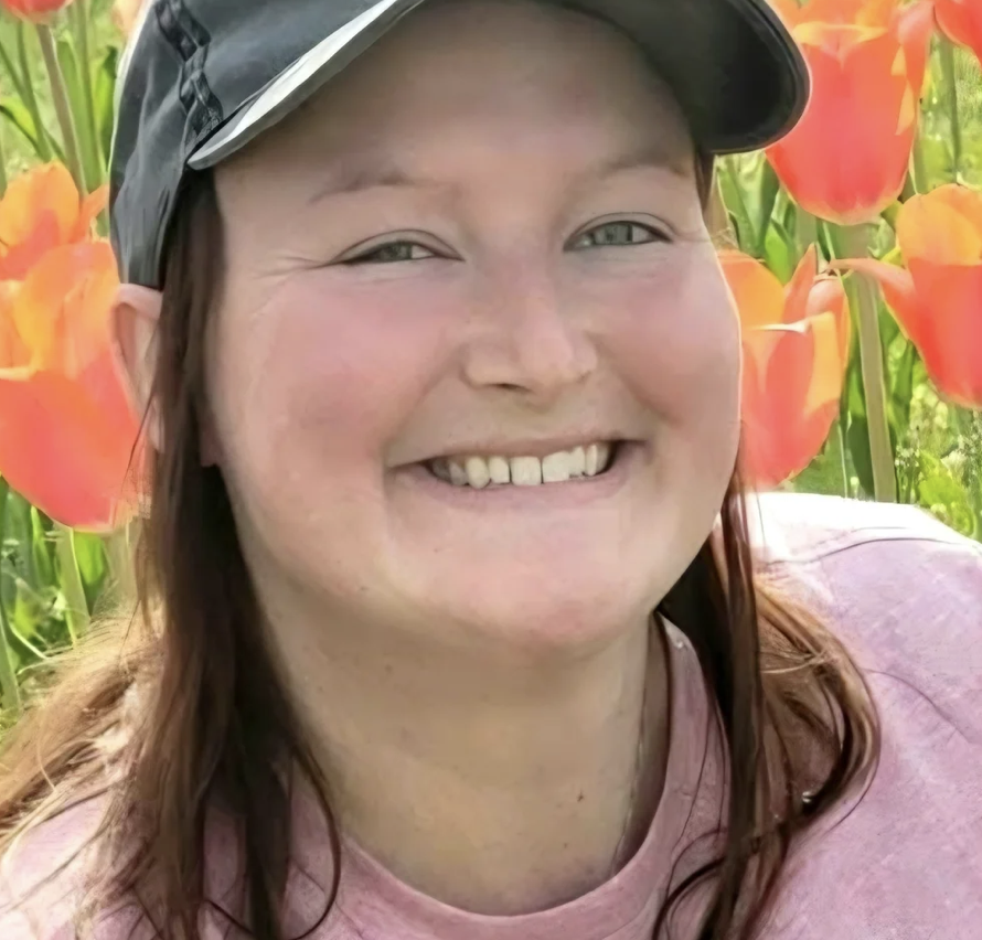 A woman smiling in a field of orange tulips, wearing a black cap and pink shirt.